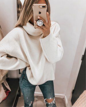 Cozy oversized white knit sweater with trendy ripped denim jeans .